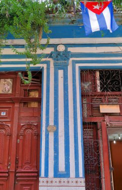 Havana, Cuba-October 27, 2019: Reddish door and white-blue striped walls in the national flag way, early 1900s Eclectic facade of tenement building at 162 Calle Habana Street, Habana Vieja-Old town. clipart