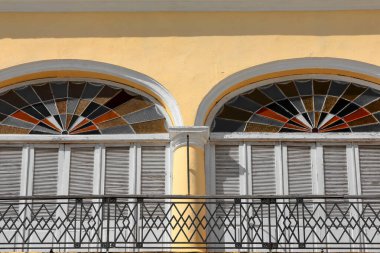 Havana, Cuba-October 27, 2019: Casa Hermanas Cardenas built c.1805 at the Plaza Vieja-Old Square NW corner, first floor balcony featuring wood louver shutters and colorful stained glass fanlights. clipart