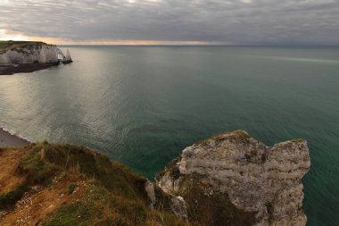 Westward view from atop the Falaise d'Amont Cliff to the rock tidal plain, the white chalk Falaise d'Aval Cliff, the wave-carved Porte d'Aval Arch, the Aiguille Creuse Needle. Etretat-Normandy-France. clipart