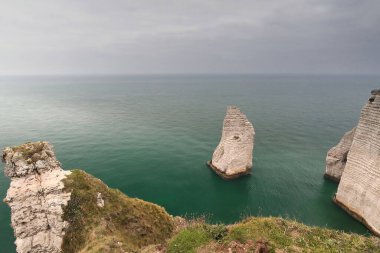 Northward view at dawn over the Plage de Jambourg Beach from atop the Falaise de la Mannerporte Cliff to the Aiguille Creuse Needle jutting from the green-turquoise calm sea. Etretat-Normandy-France. clipart