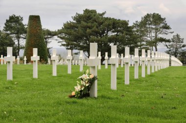 Colleville-sur-Mer, Fransa-17 Ekim 2020: Beyaz mermer haçın dibinde çiçek buketi, 2. Dünya Savaşı sırasında Avrupa 'da ölen askerler için Normandiya Amerikan Mezarlığı' ndaki bir askerin mezarının mezar taşı.