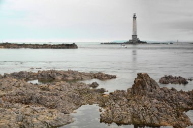 La Hague, France-October 17, 2020: Phare de Goury Lighthouse seen NW-ward from the Croix du Vendemiaire Cross area on the rocky headland hosting the Goury port. Alderney island in the far background. clipart