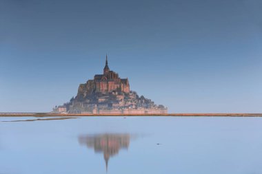 Mont-Saint-Michel, France-October 19, 2020: Northwestward view at dawn from the floodplains to the southeast of the Abbey atop a rocky tidal island seemingly floating in the air above the high tide. clipart