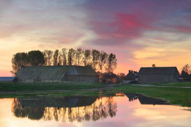 Colorful sunrise over several homesteads at the edge of the pres-sales or salt marsh meadows to the southeast of the Mont-Saint-Michel abbey, high tide flooding the flatlands while reflecting the sky. clipart