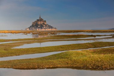 Mont-Saint-Michel, France-October 19, 2020: Northwestward view in the early morning across the floodplain to the SE of the Abbey, tidal island under a rosy-bluish light reflected in the tidal ponds. clipart