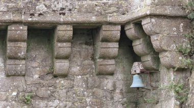 Detail of a little, old bell placed among the corbels supporting the parapet wall of a quarter-round bulwark at the foot of the refectory NE corner, Le Mont-Saint-Michel Abbey-Church. Normandy-France. clipart