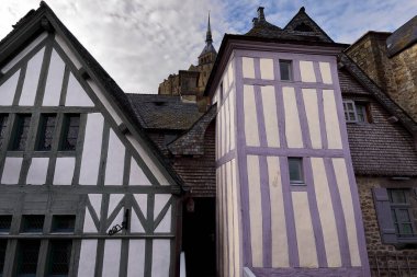 Mont-Saint-Michel, France-October 19, 2020: Half-timbered rear facades in white and green, cream and purple of XV Century buildings on the Grande Rue-Main Street overlooking the ramparts wall-walk. clipart