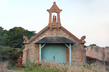 Ploumanac'h, France-October 21, 2020: The so-called Devil's Chapel, boathouse with gargoyles and a devil-like statue on the apex of the roof, on the Pink Granite Shore next to the Men Ruz Lighthouse. clipart