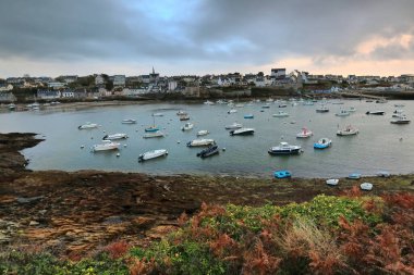 Le Conquet, France-October 23, 2020: North-to-south view of the boats moored at the ria -aber-, the port and the town from the Kermorvan Peninsula in the early evening under dark, menacing cloudy sky. clipart