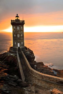 Le Conquet, France-October 23, 2020: Southwestward view in the evening of the Phare de Kermorvan Lighthouse on the westernmost tip of the homonymous peninsula, the dark sky blazing into colorful hues. clipart