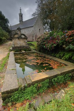 Locronan, France-October 24, 2020: Notre-Dame de Bonne Nouvelle -Our Lady of Good News- chapel from 1439, with steeple contemporary of the adjoining AD1698 fountain, all restored in the XVIII century. clipart