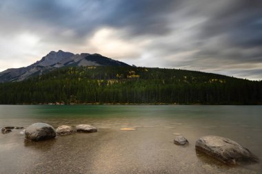 Kuzeydoğu yönünde kuzeybatı kıyısından Fairholme Sıradağları 'na kadar uzanan iki Jack Gölü' nün yeşil suyu üzerinde Inglilittle montları, sağda ve Girouard solda renkli bir sonbahar şafağında. Banff-Alberta-Kanada.