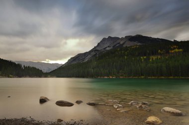 Kuzeydoğu yönünde kuzeybatı kıyısından Fairholme Sıradağları 'na kadar uzanan iki Jack Gölü' nün yeşil suyu üzerinde Inglilittle montları, sağda ve Girouard solda renkli bir sonbahar şafağında. Banff-Alberta-Kanada.