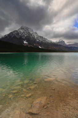 Lower Waterfowl Gölü 'nün yeşil sularından kuzeybatıya doğru bulutlarla kaplı Waputik Sıradağları' na (L-R) 3266 metre yüksekliğinde Chephren, 3094 metre yüksekliğinde Epaulette, 3110 metre yüksekliğinde Hans Kaufmann. Banff-AB-Kanada.