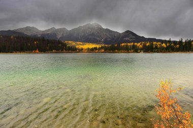 Patricia Gölü E-SE kıyısından kuzeybatıya doğru bulutlu bir öğleden sonra yeşil suları üzerinden Victoria Çapraz Dağları 'na: Piramit (sağ) ve Cairngorm (en solda). Jasper NP-Alberta-Kanada.