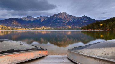 Uzun pozlama görüntüsü, Piramit Gölü ve (R-L) Piramit Dağı (2766 m) üzerinde sonbahar şafağı, Meçhul (2590 m) ve Cairngorm (2610 m), hepsi de göl kıyısındaki kayıklar tarafından çerçevelenmiştir. Jasper NP-AB-Kanada.