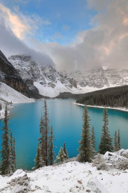On Tepe Vadisi 'ndeki Turkuaz-Mavi Moraine Gölü yoğun bir kar yağışından hemen sonra bulutlu bir gündoğumunda Rockpile Viewpoint' ten görülen ağaçlar hâlâ karla kaplı. Banff NP-Alberta-Kanada.