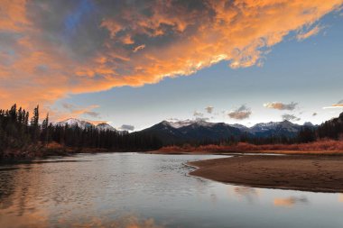 Bow River Vadisi 'nin karlı tepelerinde, Icefields Parkway' den geçen renkli akşam bulutları. Yavaş akıntısı, kırmızımsı çalılar ve kozalaklı ağaçlarla kaplı kum kütleleriyle kaplı. Banff NP-AB-Kanada.