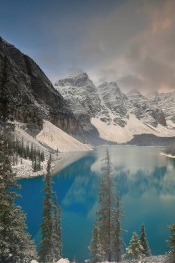 On Tepe Vadisi 'ndeki Turkuaz-Mavi Moraine Gölü yoğun bir kar yağışından hemen sonra bulutlu bir gündoğumunda Rockpile Viewpoint' ten görülen ağaçlar hâlâ karla kaplı. Banff NP-Alberta-Kanada.
