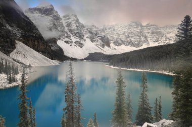 On Tepe Vadisi 'ndeki Turkuaz-Mavi Moraine Gölü yoğun bir kar yağışından hemen sonra bulutlu bir gündoğumunda Rockpile Viewpoint' ten görülen ağaçlar hâlâ karla kaplı. Banff NP-Alberta-Kanada.