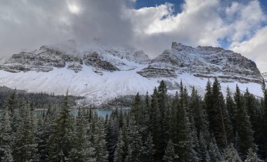 Yoğun kar yağışı sonrası bulutla kaplı olan Crowfoot Dağı (L-R) merkezi ve Bow Gölü 'nün güneybatı kıyısından yükselen kuzey bölümleri, Icefields Parkway' den görüldü. Banff NP-Alberta-Kanada.