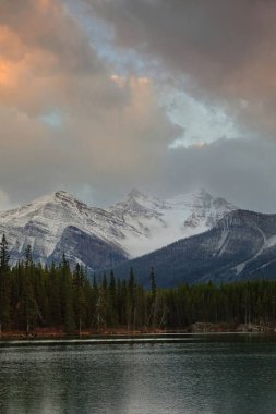 Koyu yeşil Herbert Gölü sularını geçerek kuzey kıyısından Sheol Dağı, Saddle Dağı, Haddo Tepesi, Aberdeen Dağı 'na kadar uzanır. Banff NP-Alberta-Kanada.