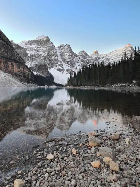 On Tepe Vadisi 'ndeki Moraine Gölü' nün zümrüt yeşili yansıtıcı suları açık mavi gökyüzünün altında bulutsuz bir gündoğumunda taşlı kuzey kıyısından güneybatıya doğru görüldü. Banff NP-Alberta-Kanada.