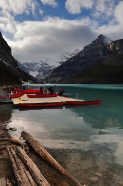 Tanınmayan maskeli insanlar -salgın zaman- Louise Gölü 'nün kıyısında yüzen bir duba üzerinde turist keyfi için kırmızı kanolar, Victoria Buzulu ve Bow Range zirveleri arkada. Banff NP-Alberta-Kanada.