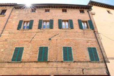 Via di Gracciano nel Corso 'nun güney tarafında yeşil boyanmış camlı panjurları ve demir çubukları olan kırmızı tuğlalı bir binanın çatısından yıldızları döküyor. Montepulciano-Toskana-İtalya.