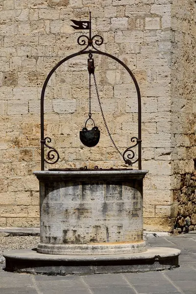 Eski kuyuda, Collegiata dei Santi Quirico e Giulitta Kilisesi 'nin yanındaki metal su toplama kovası için zincirli makara tutan paslı demir bir çerçeve vardı. San Quirico d 'Orcia-Toskana-İtalya.