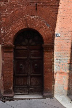 Güneş, Piazza del Popolo Meydanı yakınlarındaki Via Mazzini Caddesi 'ndeki Rönesans tarzı üç katlı bir konağın batıya bakan kırmızı tuğla cephesine ışık ve gölge oyunları sergiliyor. Montalcino-Toskana-İtalya.