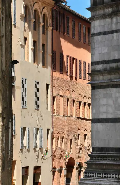 Siena, İtalya-12 Mayıs 2022: Via dei Pellegrini Caddesi 'nin başındaki Ortaçağ ve Rönesans tarzı binalar, Via Fusari Caddesi' nin sonundaki kemerden Piazza San Giovanni Meydanı 'na doğru görüldü..