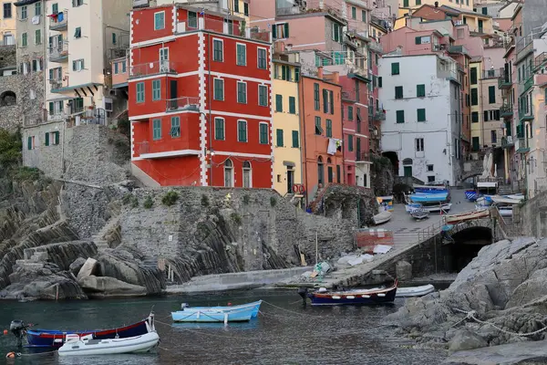 Riomaggiore, İtalya-12 Mayıs 2022: Dik yamaçtaki renkli binaların üzerinden gün doğumu sahile iniyor, yerel tekneler hala küçük limanda demirli ve kıyıda..