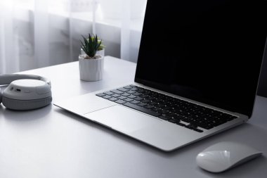 Ultrabook dizüstü bilgisayar, fare, müzik kulaklıkları ve beyaz masa arka planındaki bitkilerin yan görüntüsü. Uzak bilişim işi için ev ofisi kavramı.