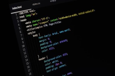 Karanlık temalı bir kod düzenleyicide HTML ve CSS kodlarını gösteren bir bilgisayar ekranının makro fotoğrafı. Parçacık, tanımlanmış yazı tipleri, renkler ve düzen özelliklerine sahip biçimlendirilmiş bir web sayfası yapısını gösterir. Ön uç geliştirme ile ilgili temalar için mükemmel, kod. 