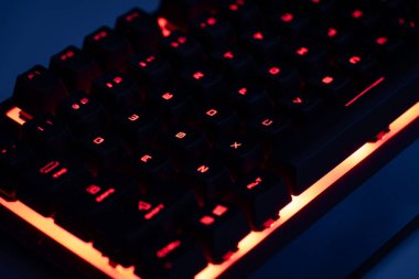 Karanlık odada aydınlatılan renkli bir oyun klavyesinin yakın çekimi. Oyuncu kırmızı arka farlı bilgisayar mekanik klavyeyi kuruyor. Oyun için tasarlanmış modern bilgisayar aksesuarı, özelleştirilmiş arka ışıklandırma ve şık tasarım. 