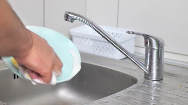 若い男が石鹸とスポンジで家で料理を洗います 男は毎日皿を洗う 資源の非合理的な消費の概念 — ストック動画