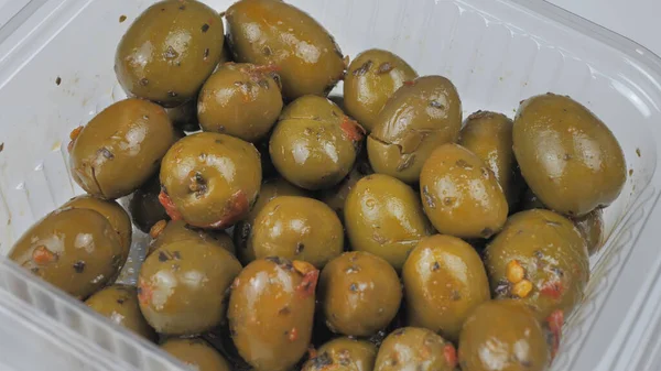 green pickled olives close-up in a transparent container.