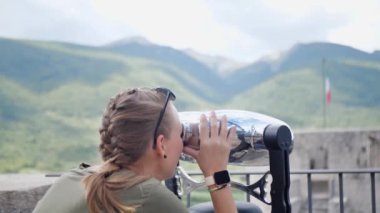 Güzel manzaraya büyük sokak dürbünlerinden bakan genç bir kadın. Turist kız deniz, orman ve dağlarla manzarayı izlemek için izleme makinesi kullanıyor. Teleskopla izleyen kadın.