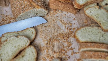 Whole grain bread close-up on the wooden cutting board. Knife with serrated blade. Fresh bread on the wooden kitchen table. Flat lay with traditional pastries in bakery