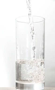Kırpma yolu ile beyaz arkaplanda izole edilmiş bardağa su dökün.