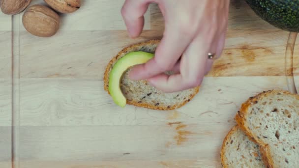 Θηλυκό Χέρι Βάζει Κομμάτια Αβοκάντο Στο Ψωμί Μια Ξύλινη Σανίδα — Αρχείο Βίντεο