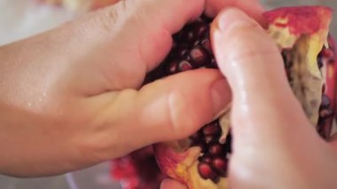 Kadın elleri, masada bir tabağın üzerinde bir nar temizler. Bir kadın mutfakta sulu taze bir nar yemeye hazırlanıyor. Sağlıklı beslenme ve veganlık kavramı