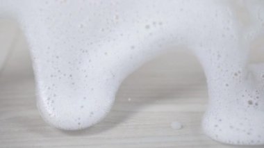 Beyaz sabun köpüğü cam duvar arka planında akıyor.