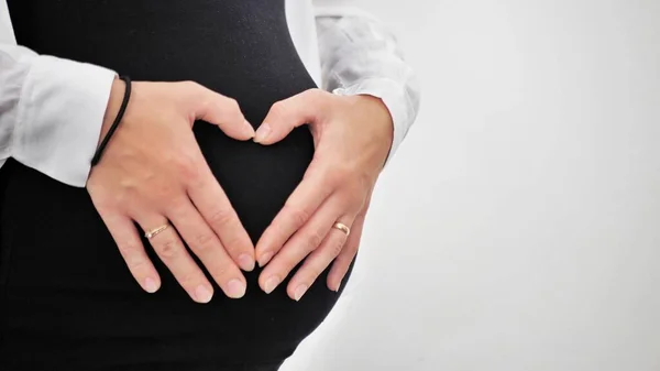 妊娠中の女性は赤ん坊のバンプの心臓の形で彼女の手を握っている 妊娠中の腹指ハートシンボル 妊娠の概念 ベビーシャワー — ストック写真