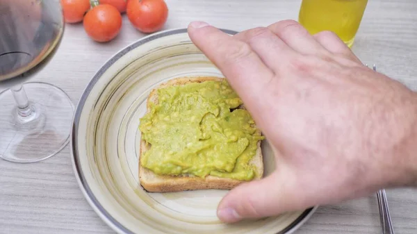 a mans hand takes toast with mashed avocado from a plate. framing shot. Concept of healthy vegan food. Avocados are rich in healthy saturated fats.