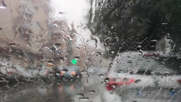 雨が車のフロントガラスビューに落ちる 交通渋滞の通りに激しい雨の嵐で車を運転し 車の運転中に ぼやけた交通光の背景 — ストック動画