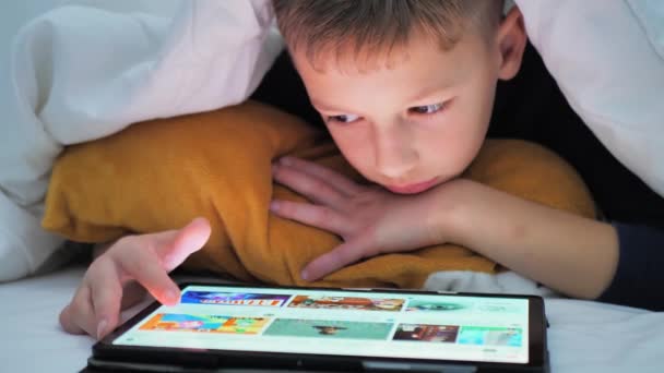 Kleiner Junge Spielt Auf Tablet Während Unter Decke Liegt Cartoons — Stockvideo