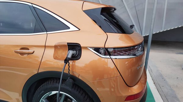 Крупный план электрического зарядного устройства автомобиля с женским силуэтом на заднем плане.