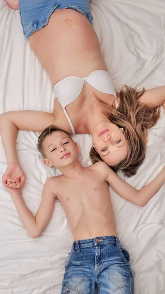 Küçük bir oğlan ve hamile annesi yatakta birlikte yatıyorlar. Aile eğlencesi. Yumuşak odak.